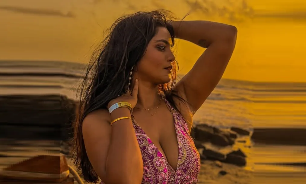 232ee Woman with long dark hair in a pink paisley halter top posing on a rocky beach at golden sunset