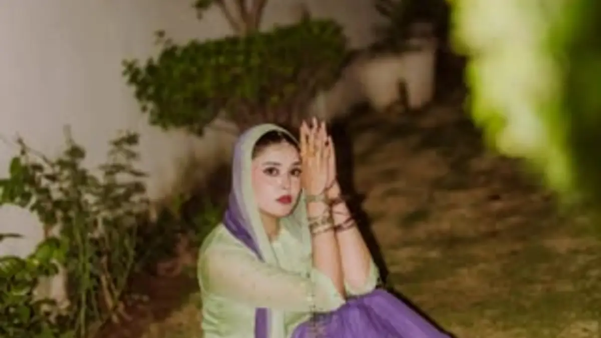 kanwal-aftab-featured Woman in a mint-green outfit and lavender scarf sits outdoors at dusk, palms pressed together near a white wall