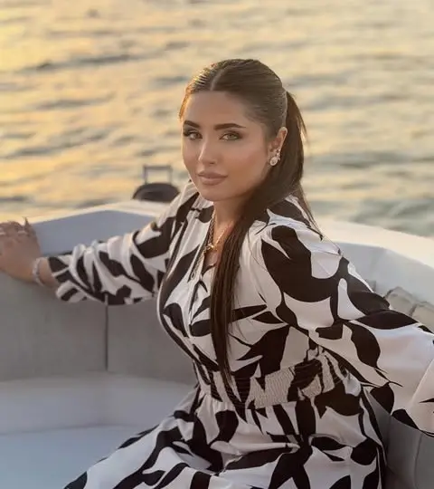 Woman with a low ponytail in a black-and-white leaf-print dress, seated on a white boat at sunset